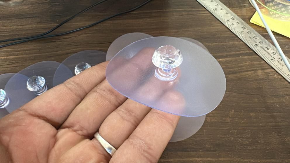 Hand holding a clear suction cup on a wooden surface with a ruler in the background