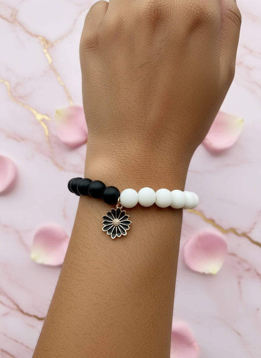 Black and white beaded bracelet with a floral charm on a light gray background